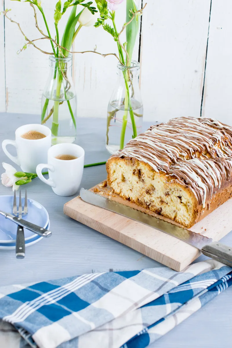 Ein Stück Kinderschokolade Kuchen auf einem Teller, mit Gabel und einem weiteren unangeschnittenen Kuchen im Hintergrund
