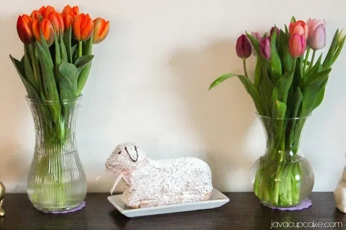 Ein wunderschön bestäubtes Osterlamm auf einem Tisch, umgeben von Kaffeetassen und Frühlingsdekoration