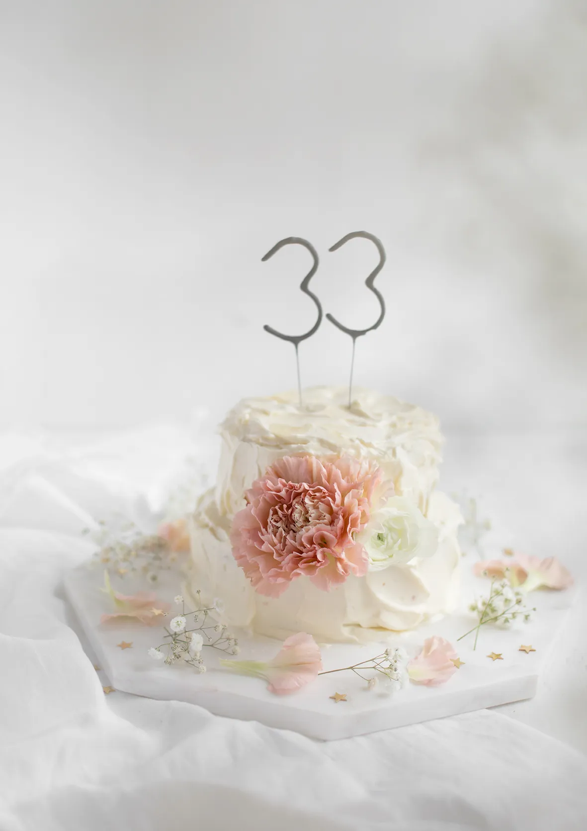 Ein zweistöckiger Geburtstagskuchen, verziert mit frischen Blüten und Wunderkerzen, für den 33. Geburtstag