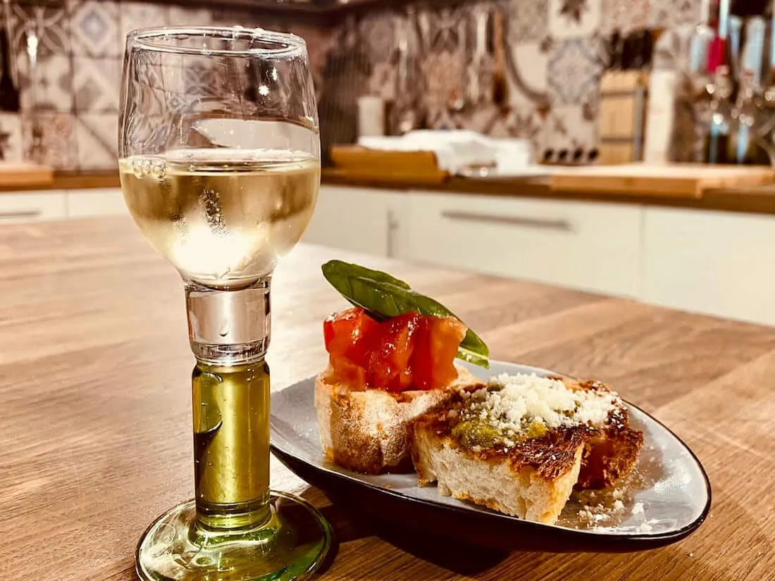 Eine Auswahl köstlicher Bruschetta-Häppchen mit frischen Tomaten und Basilikum, daneben ein Glas Weißwein