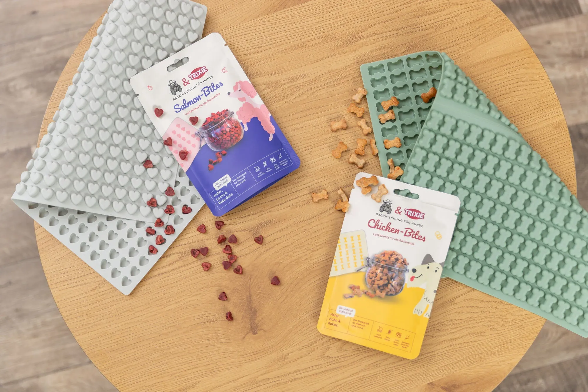 Eine Auswahl von TRIXIE Pets Kitchen Backmischungen für Hundekekse, Chicken Bites und Salmon Bites, zusammen mit Silikon-Backmatten in Herz- und Knochenform und fertigen Leckerlis.