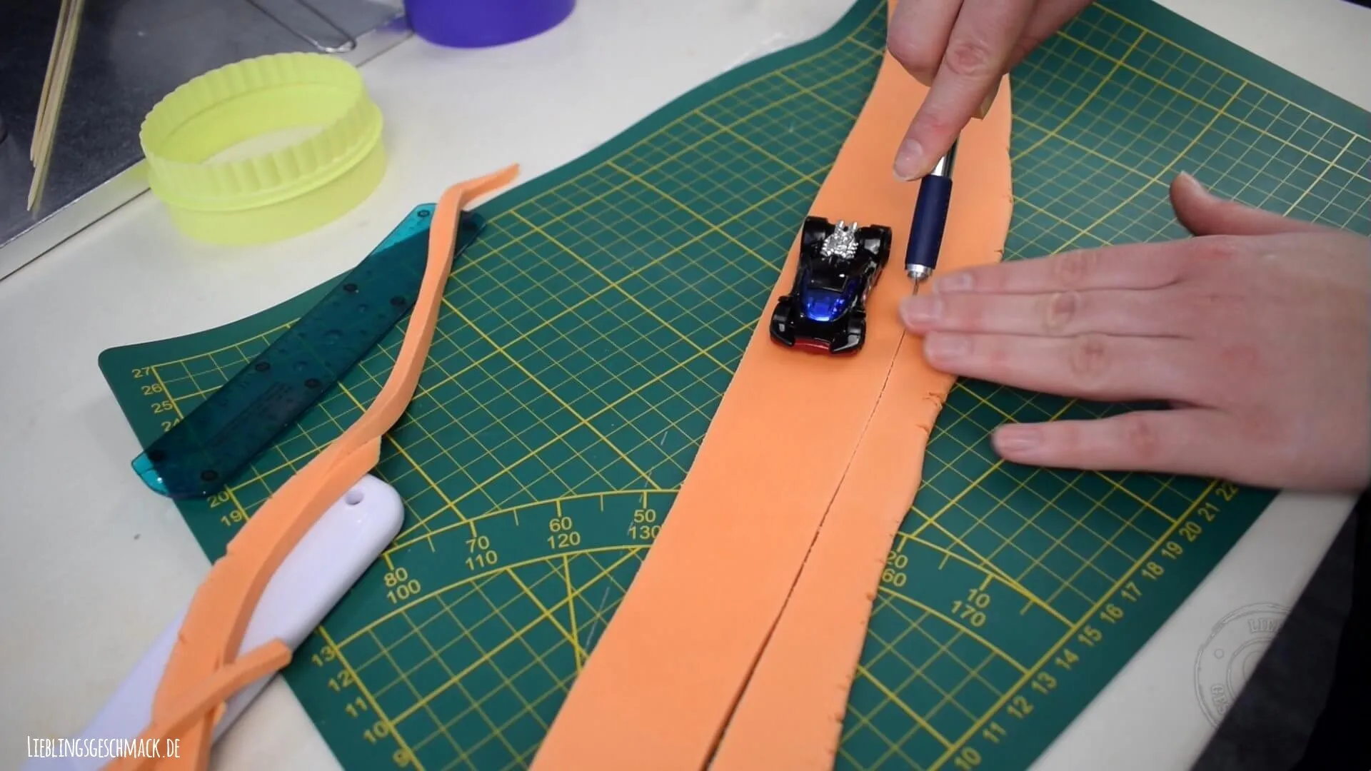 Eine Bahn aus oranger Blütenpaste wird für den Looping zugeschnitten, der später die Hot Wheels Autos tragen wird