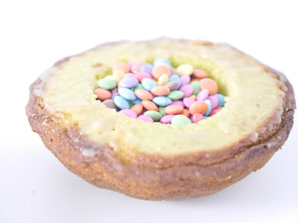 Eine Hand füllt die Mulde eines ausgehöhlten Kuchenteils großzügig mit bunten Smarties.