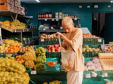 Eine junge Frau kauft frisches Obst und Gemüse auf einem Markt ein, symbolisiert ethischen Konsum und nachhaltige Lieferketten.