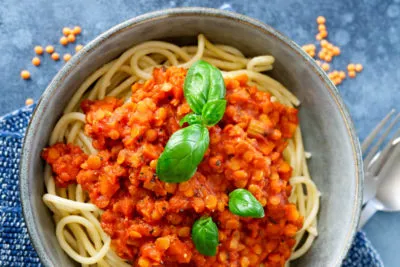 Eine köstliche rote Linsen Bolognese, fertig serviert mit frischem Basilikum und klassischen Spaghetti.