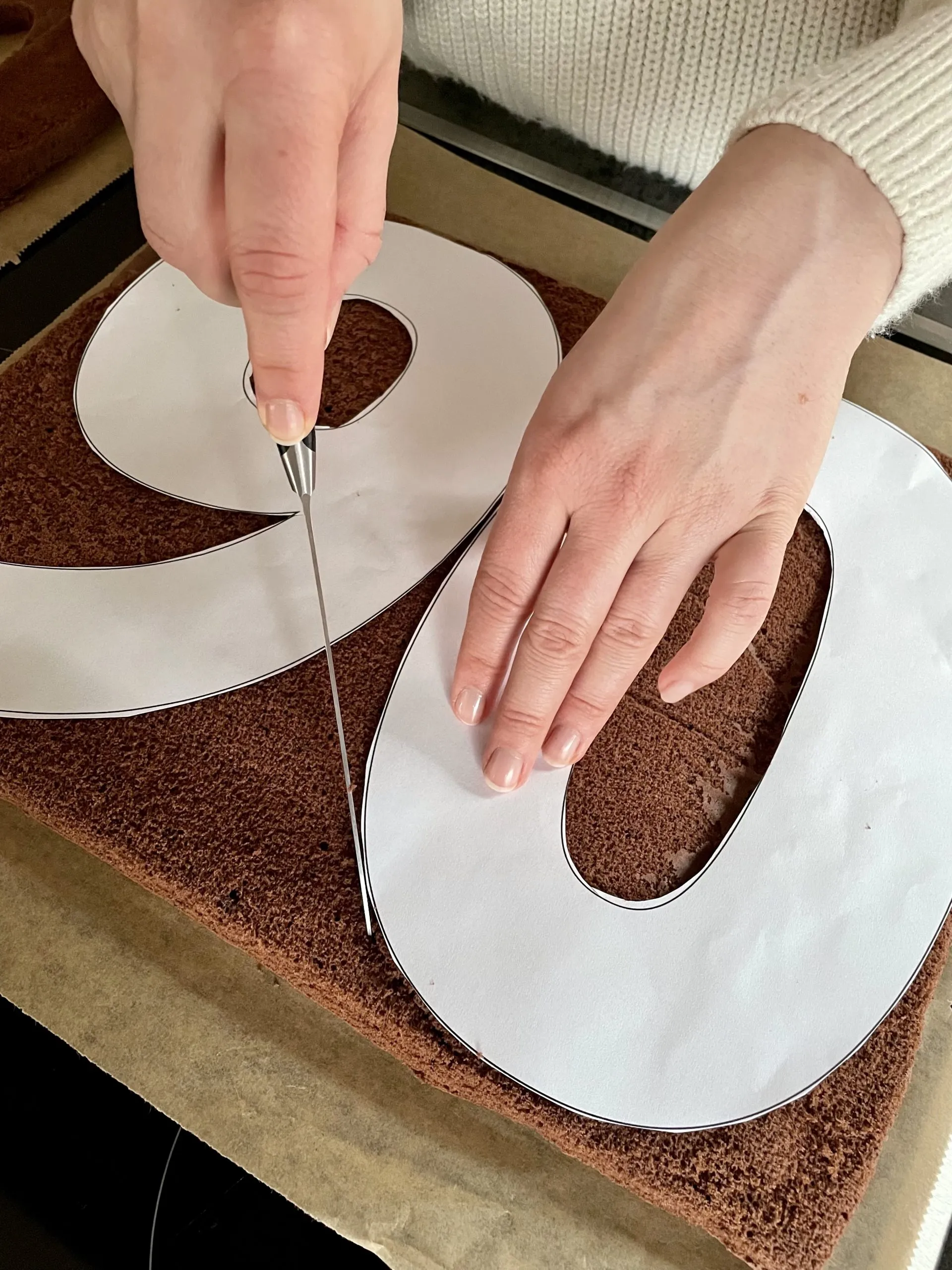 Eine Küchenszene zeigt das Ausschneiden der Zahl aus dem gebackenen Biskuitboden mit einer Schablone