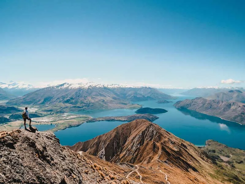 Eine malerische Berglandschaft in Neuseeland mit einem Fluss, der sich durch eine grüne Ebene schlängelt, unter einem blauen Himmel