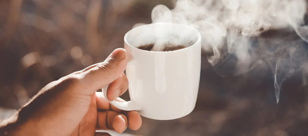 Eine Person hält eine Tasse heißen, schwarzen Kaffee in der Hand, der dampft.