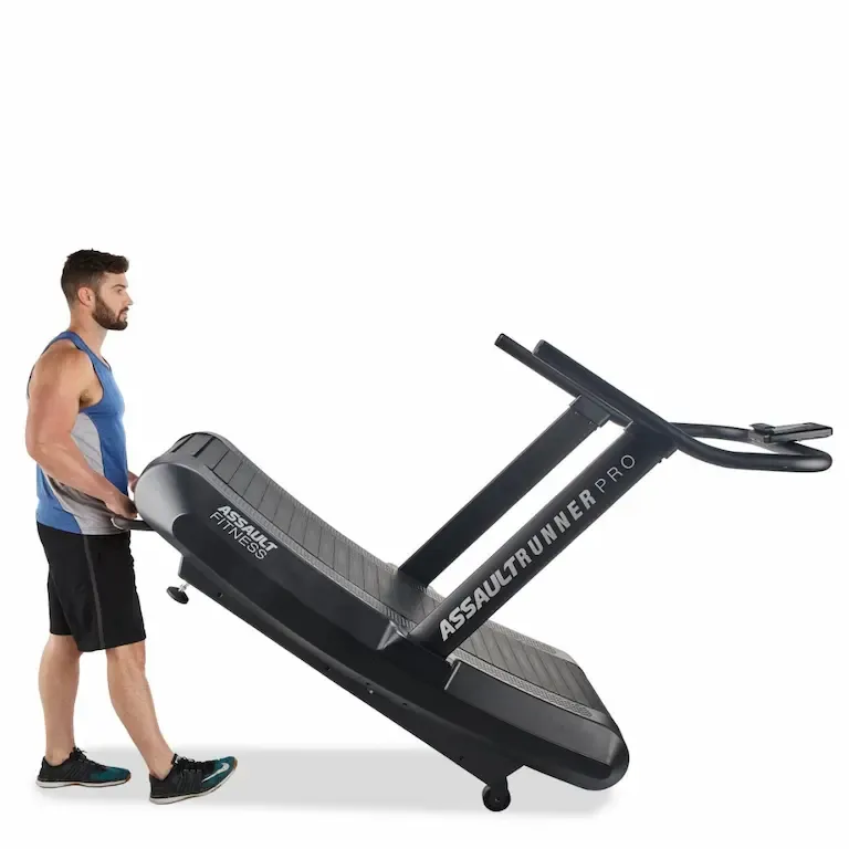Eine Person schiebt das Assault Laufband AirRunner Pro mittels des Hebegriffs und den Transportrollen, die an der Vorderseite des Geräts angebracht sind.