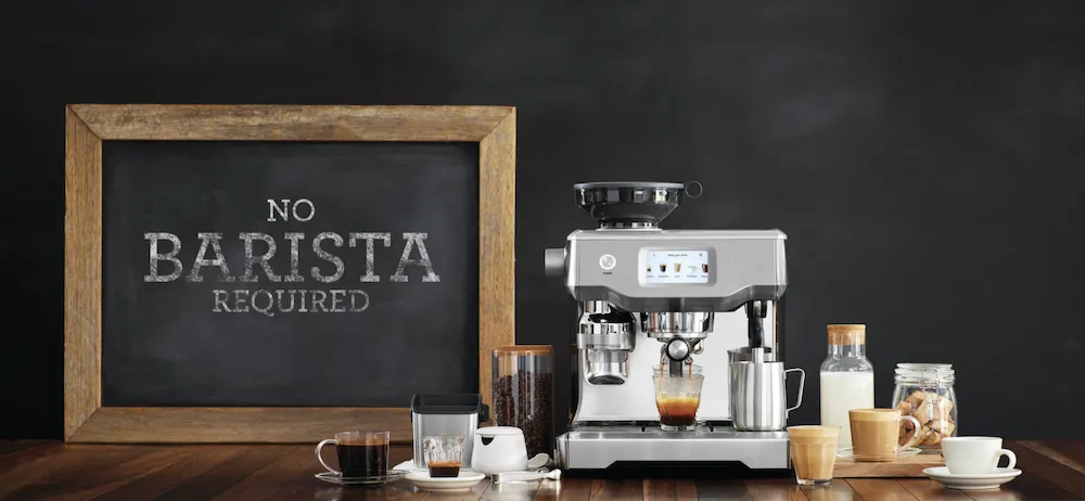 Eine Sage Siebträgermaschine auf einem gedeckten Frühstückstisch mit Kaffee und Gebäck.