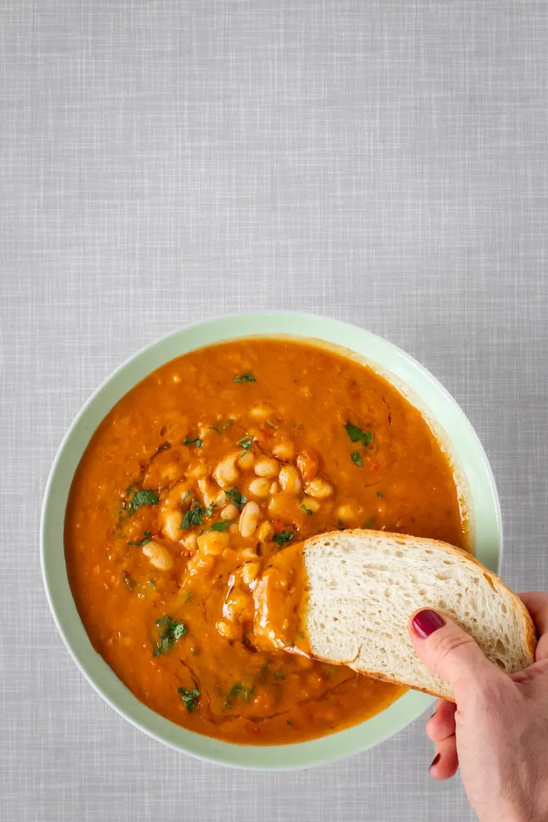 Eine Scheibe Weißbrot wird in eine cremige albanische weiße Bohnensuppe getaucht.