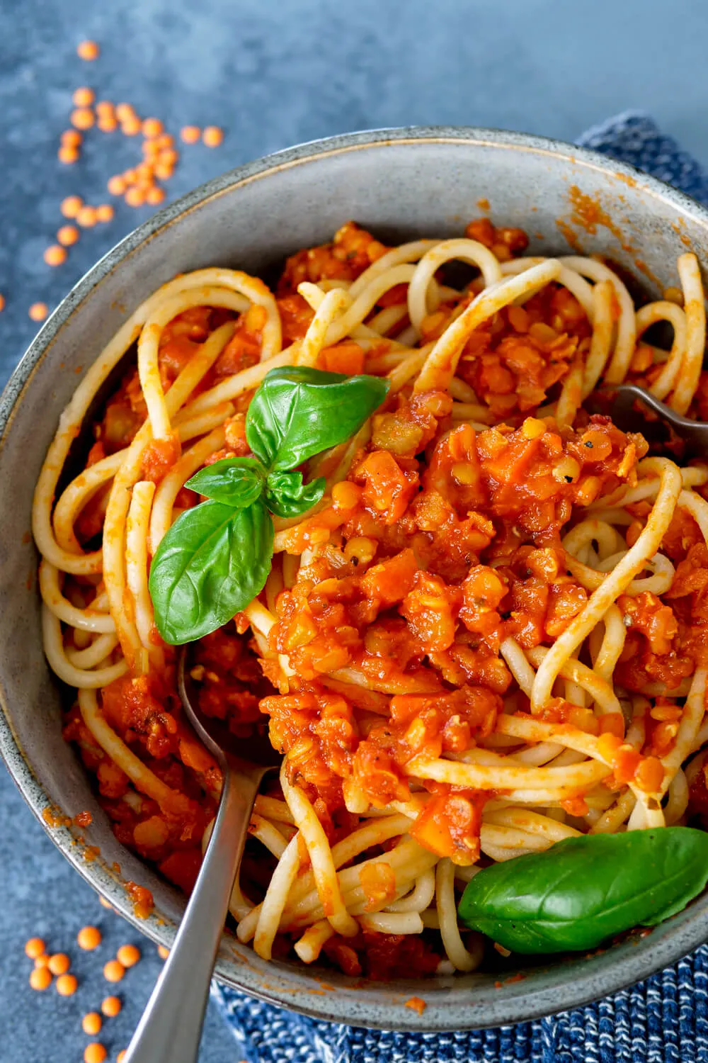Eine Schüssel voller cremiger roter Linsen Bolognese mit Spaghetti und frischem Basilikum, ideal für die ganze Familie.