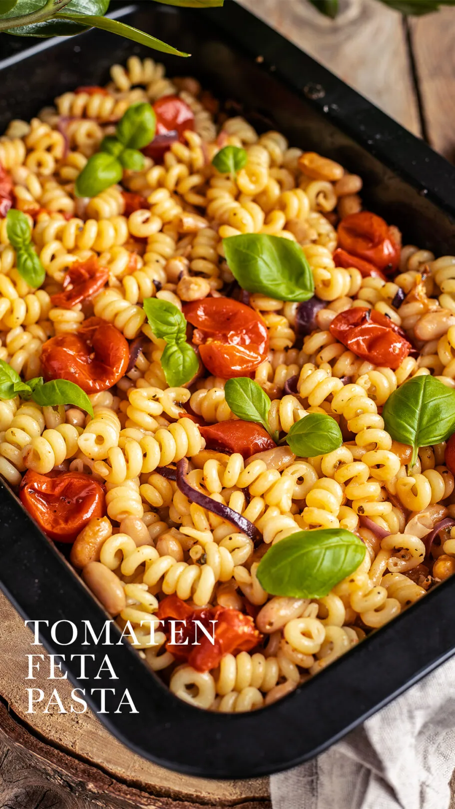 Eine schwarze Auflaufform mit einer leckeren veganen Tomaten Feta Pasta, garniert mit frischem Basilikum.