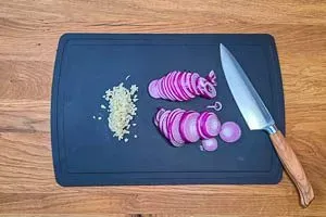 Fein gewürfelte Knoblauchzehen und in dünne Scheiben geschnittene rote Zwiebeln, vorbereitet für den Kritharaki-Auflauf