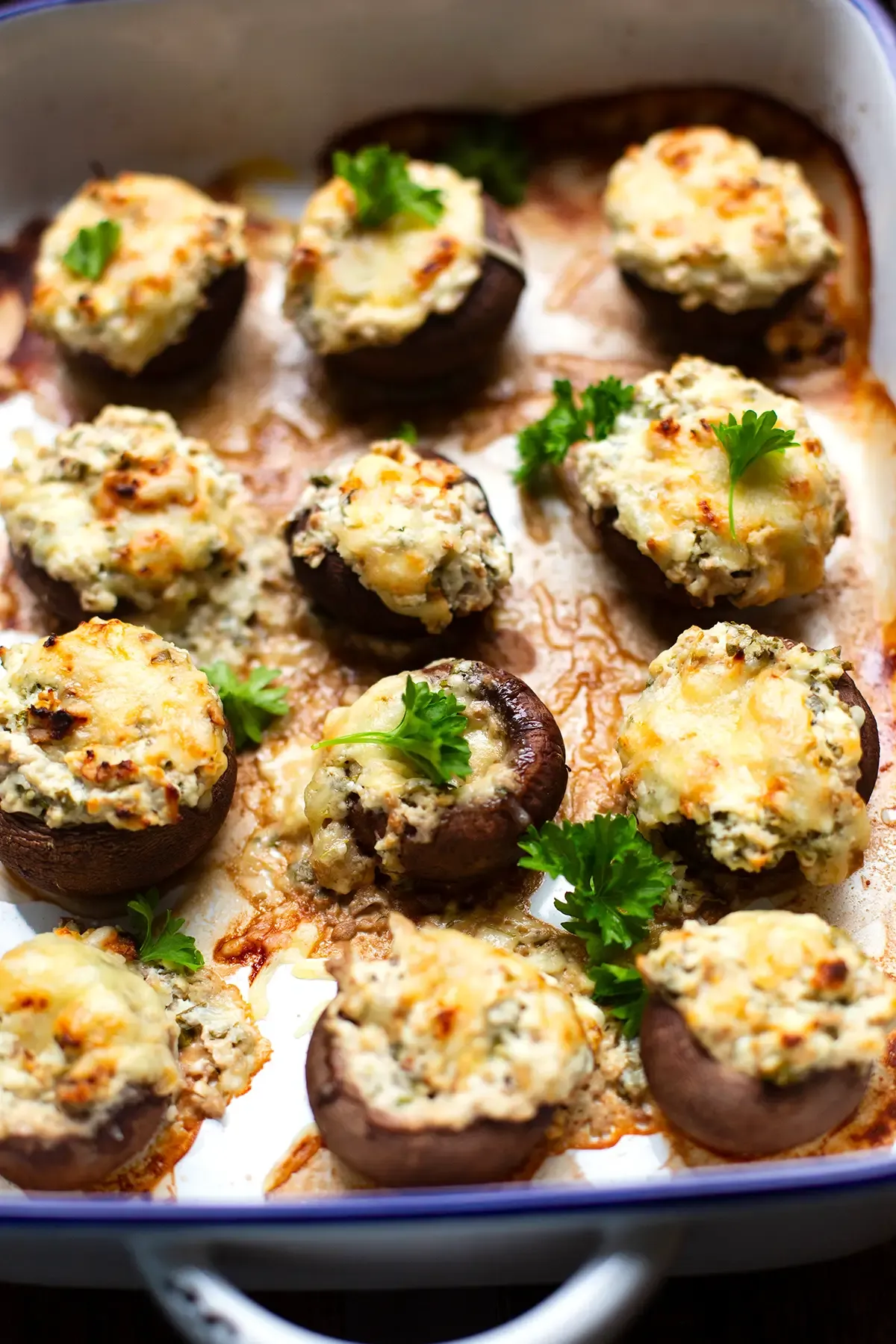 Fertige vegetarisch gefüllte Champignons in einer weißen Auflaufform, garniert mit frischer Petersilie
