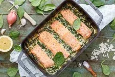 Fertiger Lachs-Spinat-Auflauf mit Zitronenspalten und Kräutern garniert, servierfertig
