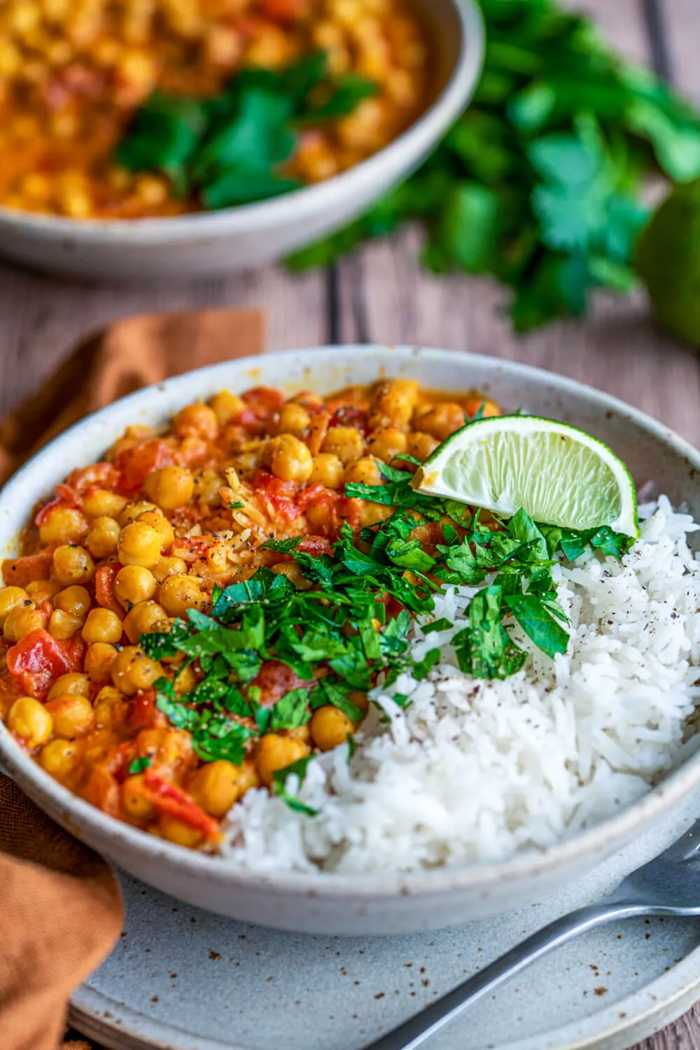 Fertiges Kichererbsen-Curry mit Reis auf einem weißen Teller, garniert mit frischer Limette und Kräutern