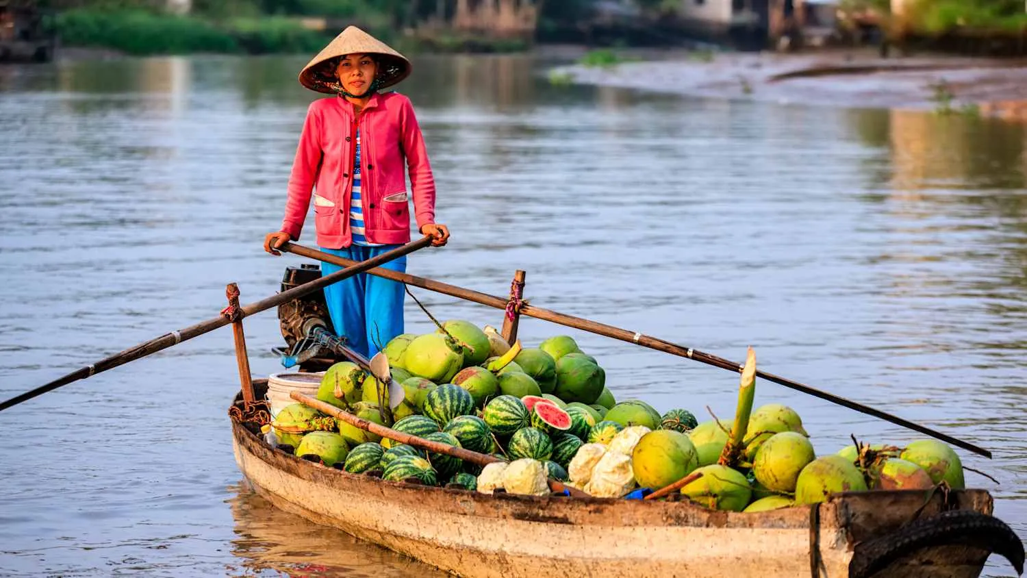 Frau fährt ein traditionelles Holzboot beladen mit Wassermelonen und Kokosnüssen auf den weitläufigen Wasserwegen des Mekong-Deltas in Vietnam