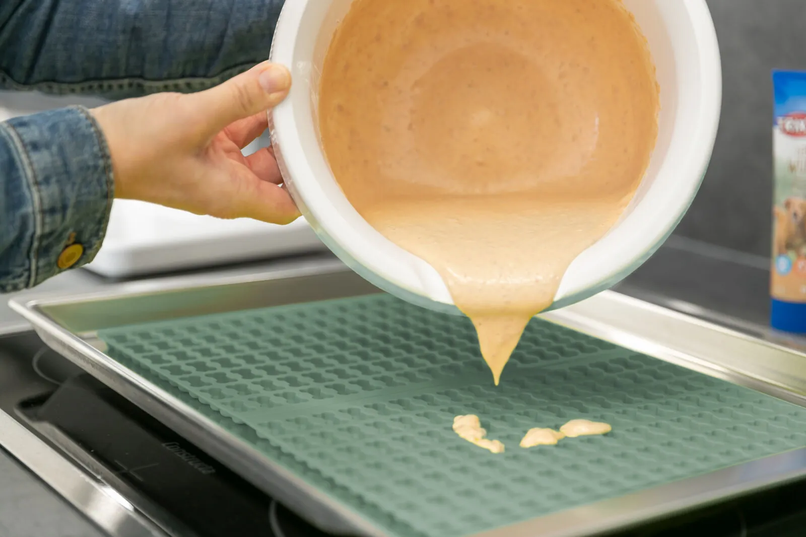 Frisch gebackene Hundekekse in Knochen- und Herzform auf einer Silikon-Backmatte, umgeben von weiteren Backmatten auf einem Backblech, bereit zum Abkühlen.