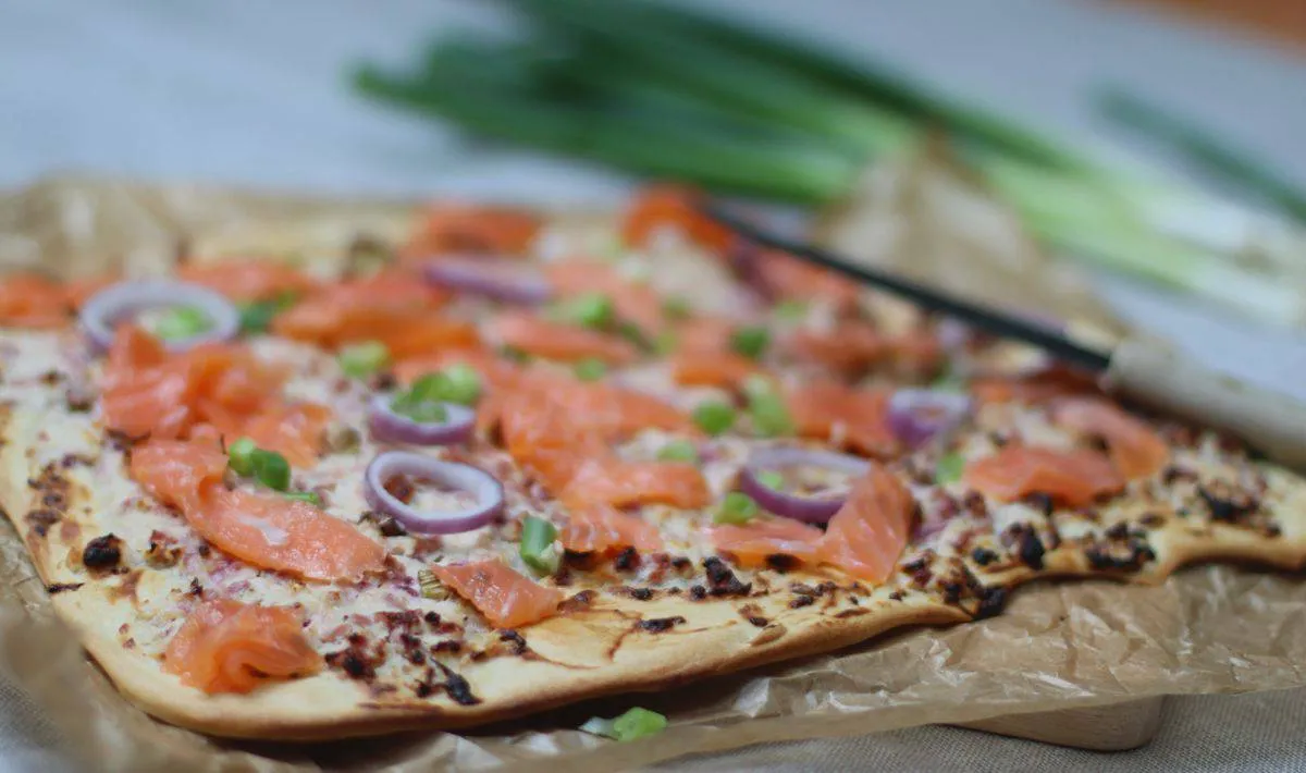 Frisch gebackener Flammkuchen mit Räucherlachs, Frühlingszwiebeln und Schmand