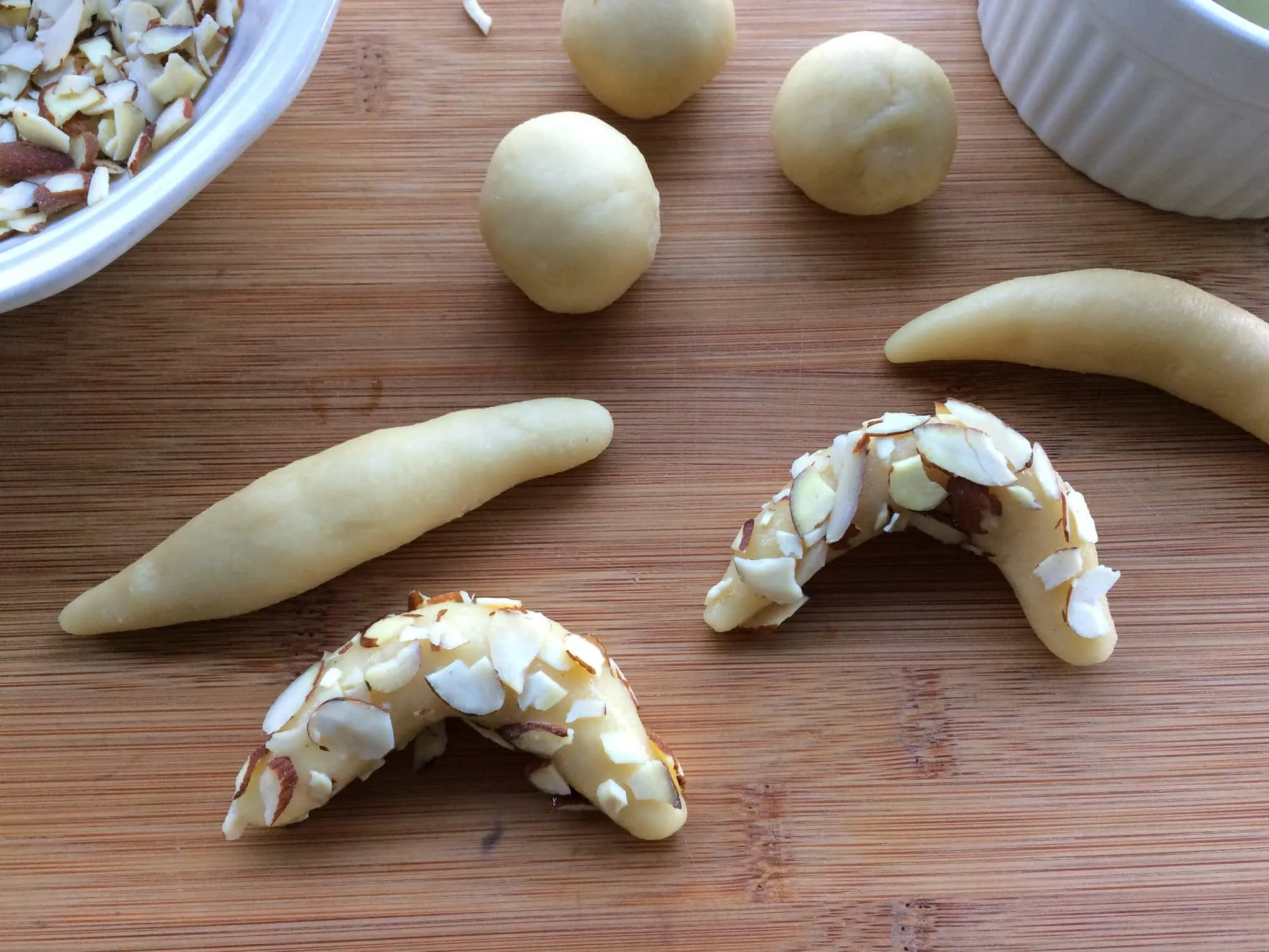 Geformte Mandelhörnchen vor dem Backen mit Mandelsplittern bedeckt