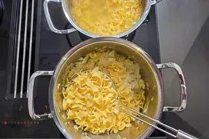 Gekochte Fleckerl-Nudeln werden zum geschmorten Kraut in den Topf gegeben