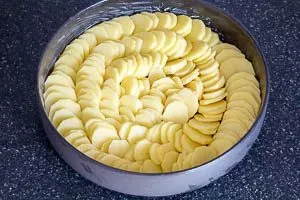 Geschälte Kartoffeln werden in dünne Scheiben geschnitten und spiralförmig in eine runde Auflaufform geschichtet
