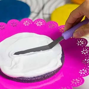 Geschichteter Regenbogenkuchen mit veganer Sahne zwischen den farbigen Böden, bereit zum Frosten