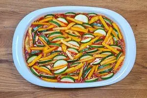 Gleichmäßig verteilte Paprikastreifen und Zucchinischeiben werden auf der Kritharaki-Hackfleisch-Mischung in der Auflaufform geschichtet