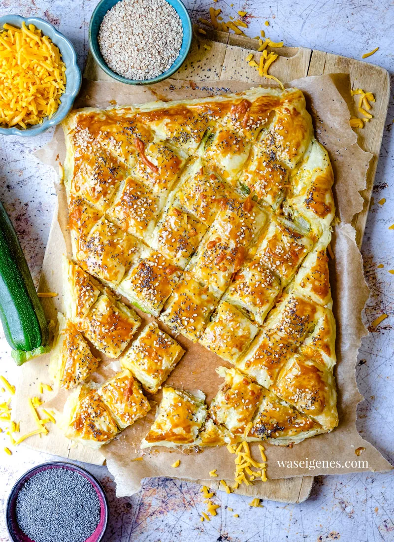 Goldbraunes Blätterteig-Zupfbrot mit Zucchini und Cheddar auf einem rustikalen Holzbrett