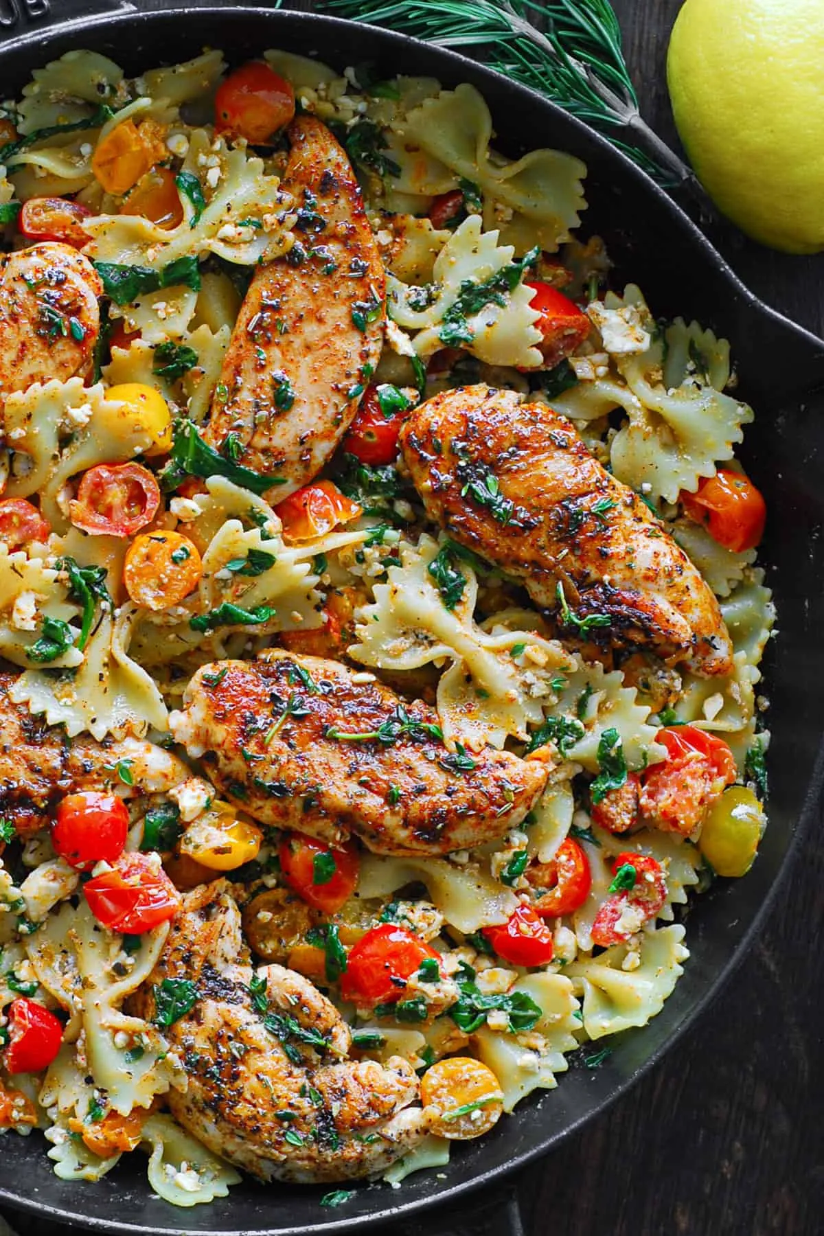 Hähnchen-Feta-Pasta in einer gusseisernen Pfanne, geschwenkt mit Schleifchennudeln, frischen Tomaten und Spinat.