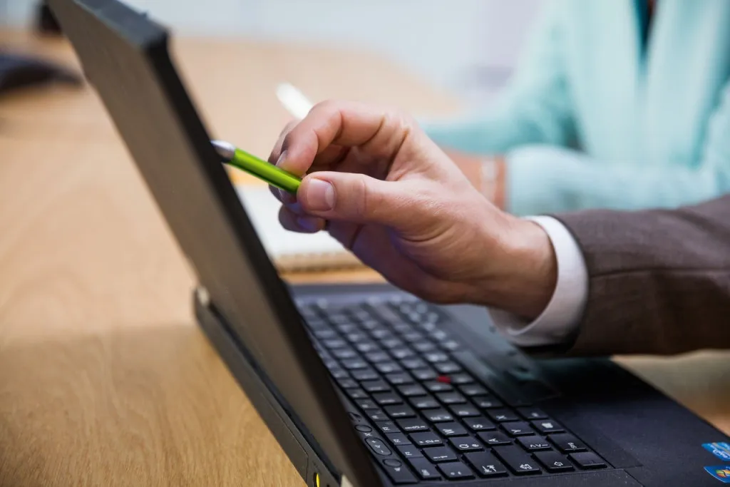 Hand mit DATEV Kugelschreiber zeigt auf Laptop-Bildschirm bei der Suche nach BMD DATEV Schnittstellen für die digitale Buchhaltung