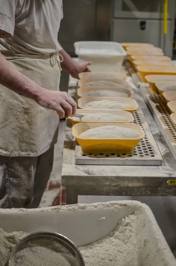 Hände eines Bäckers ritzen sorgfältig Muster in Brotteige, ein Zeichen traditioneller Handwerkskunst.