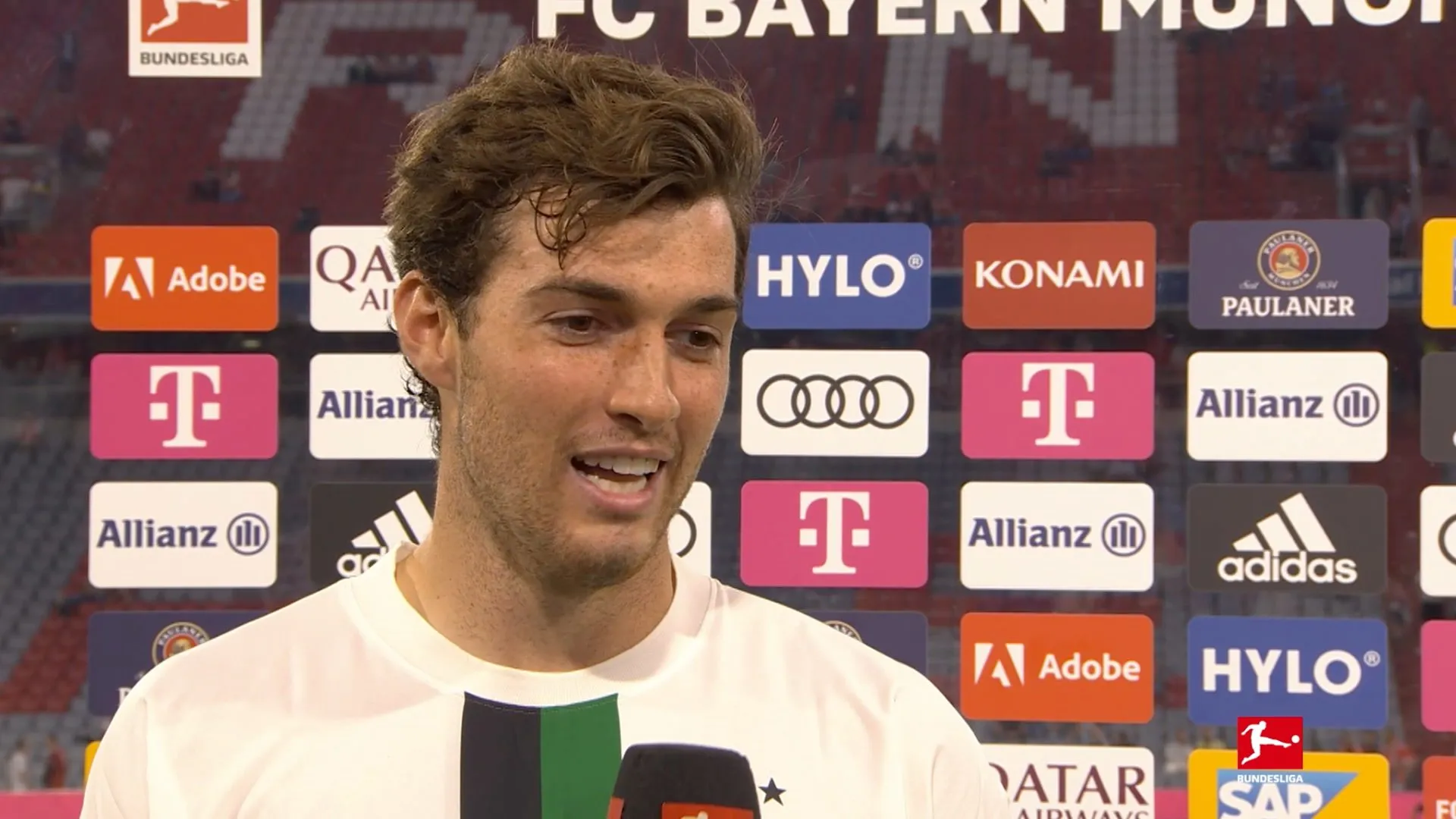 Joe Scally im Interview, im Hintergrund das Spielfeld des Stadions