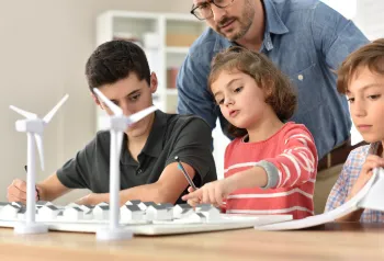 Kinder sitzen vor einem Windrad-Modell und lernen über erneuerbare Energien