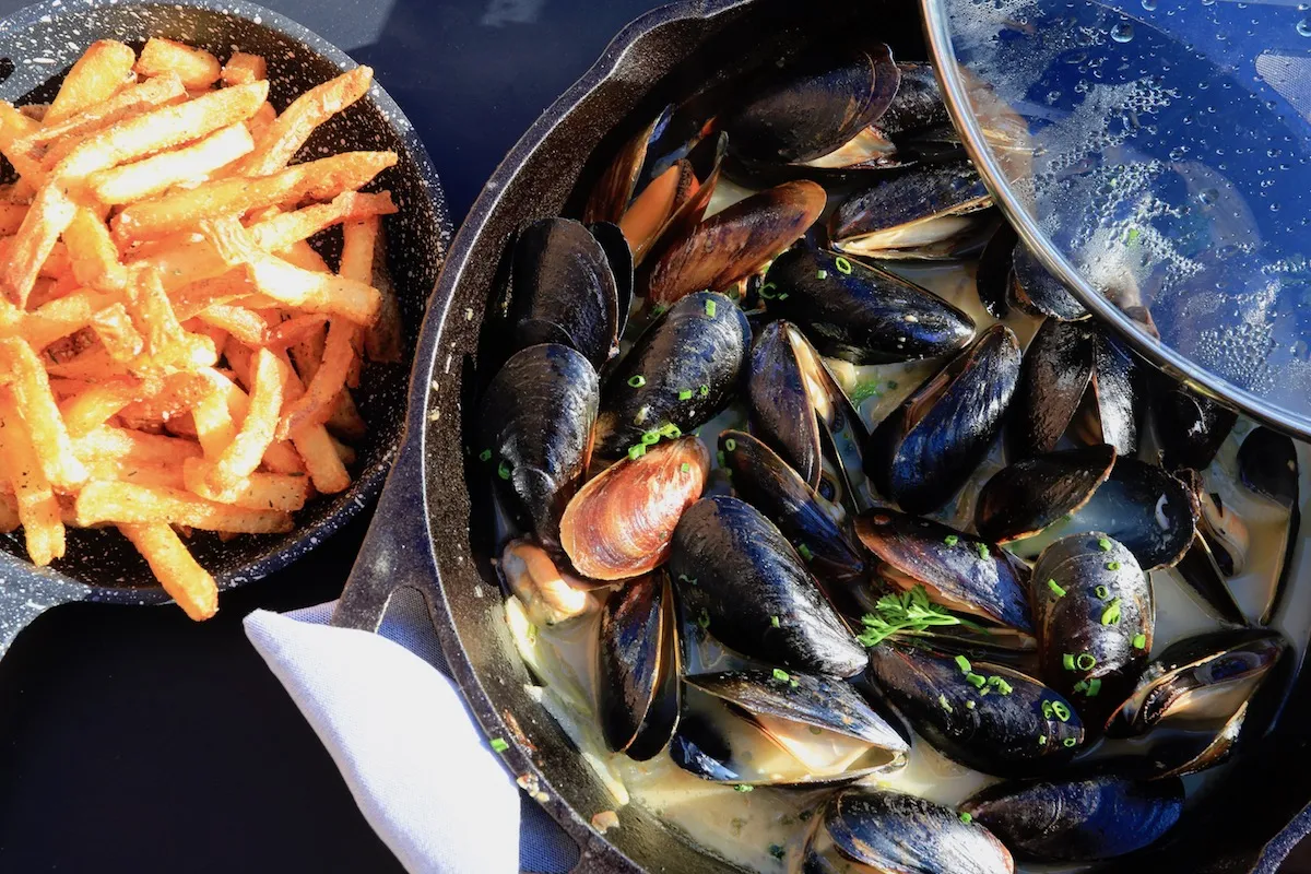 Klassische Moules Frites mit goldbraunen Pommes, angerichtet in der Brasserie Liberté