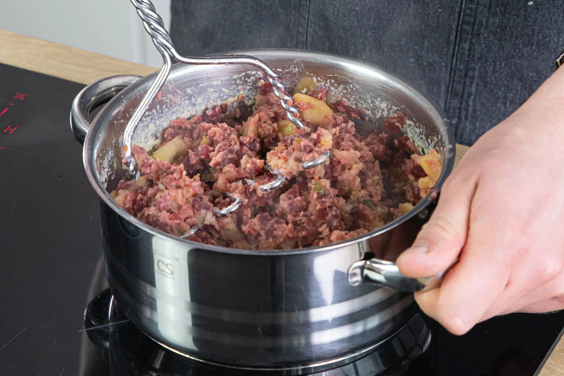 Labskaus-Masse mit Kartoffelstampfer zerkleinern