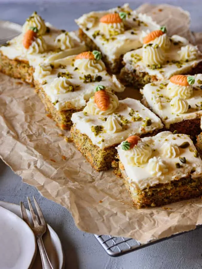 Mehrere Stück Blechkuchen aus Karotten-Mohn-Teig auf Backpapier, auf einem Kuchengitter