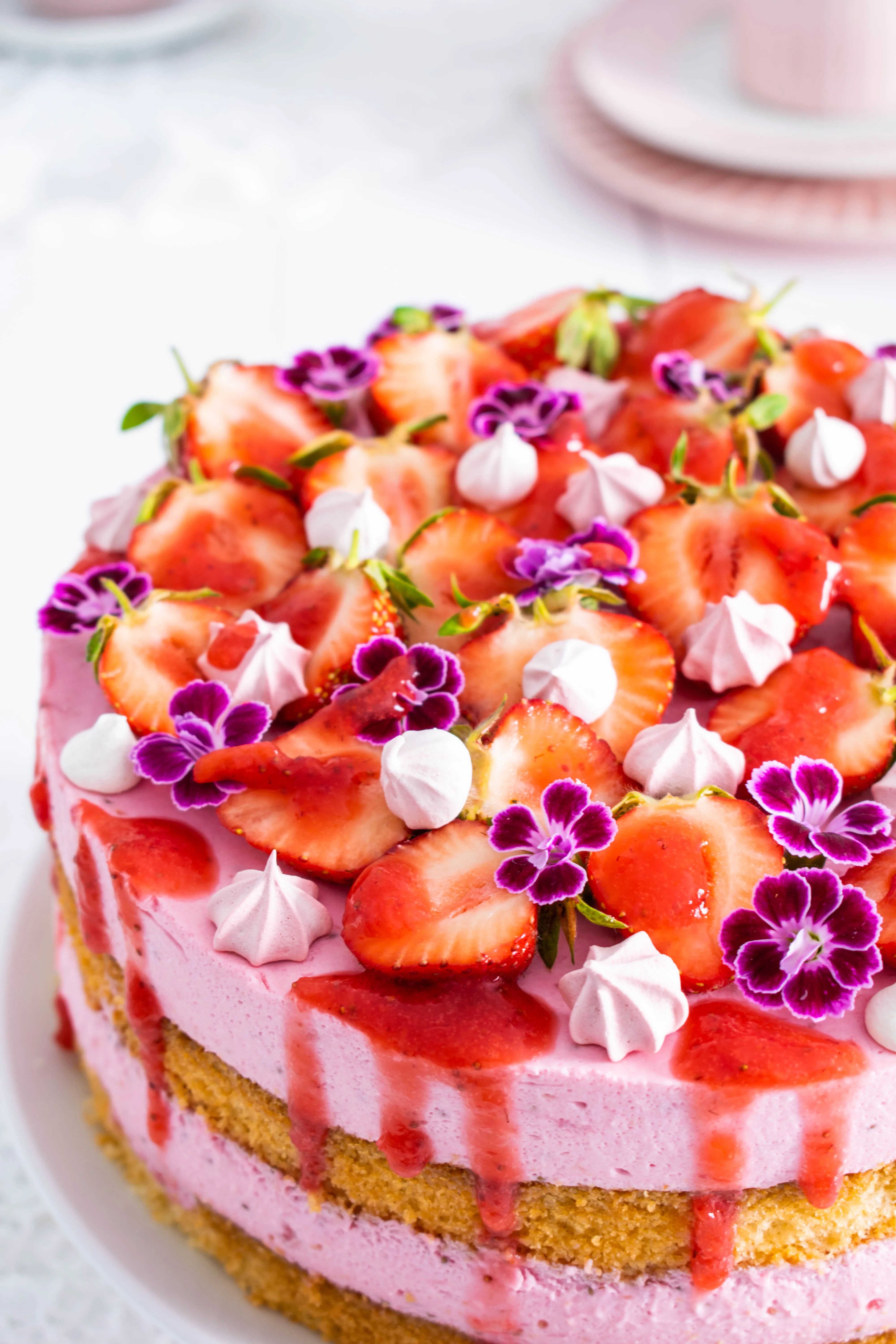 Nahaufnahme einer cremigen Erdbeersahnetorte, von oben dekoriert mit halbierten Erdbeeren und Baiserstückchen