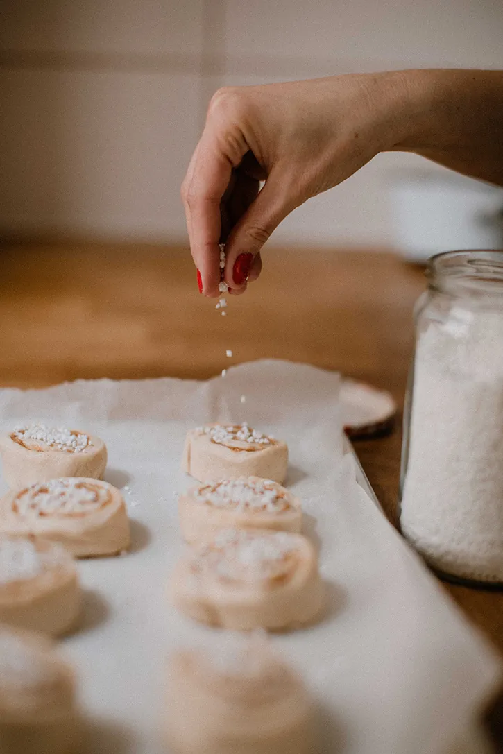 Nahaufnahme einer frisch gebackenen, glasierten Zimtschnecke auf einem Backpapier, perfekt für den Kaffeetisch.