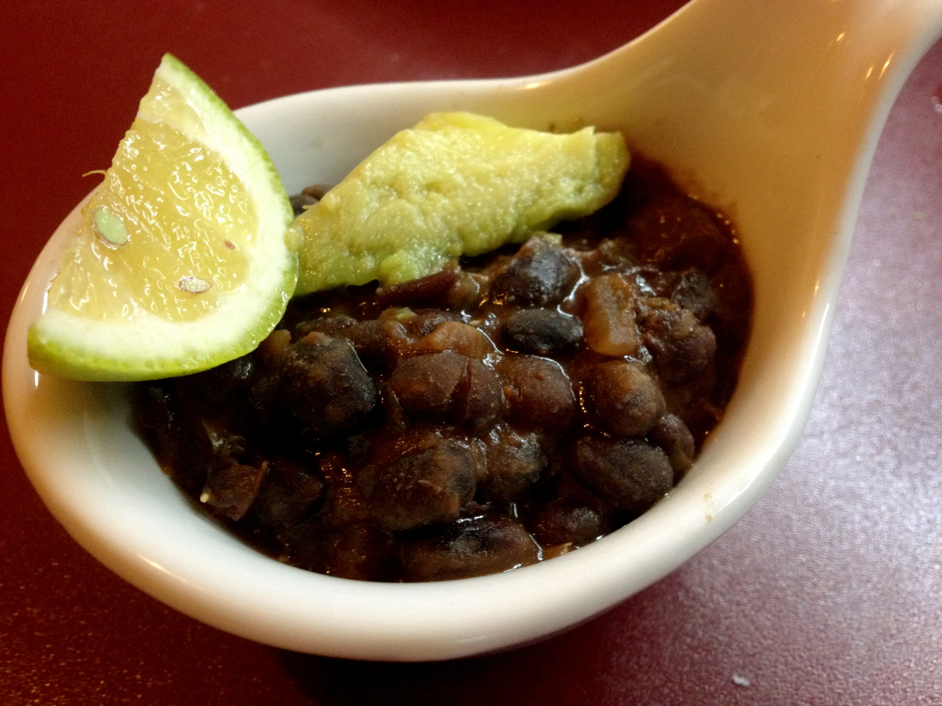 Nahaufnahme einer Portion schwarzer Bohnen mit frischen Korianderblättern und Limettenspalten
