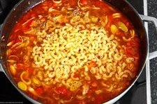 Nudeln und Brühe werden dem Hackfleisch und Gemüse in der Pfanne hinzugefügt