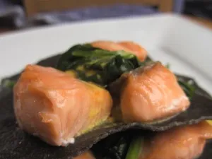 Offene Spinat Lachs Lasagne mit schwarzem Nudelteig und Safran-Orangensauce, fertig angerichtet auf einem Teller.