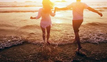 Paar spaziert Hand in Hand durch die blühende Lüneburger Heide bei Sonnenuntergang