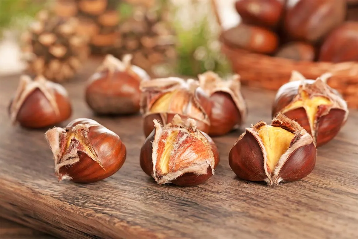 Perfekt geröstete Maronen mit aufgeplatzter Schale, appetitlich angerichtet auf einem rustikalen Holztisch, bereit zum Genuss.