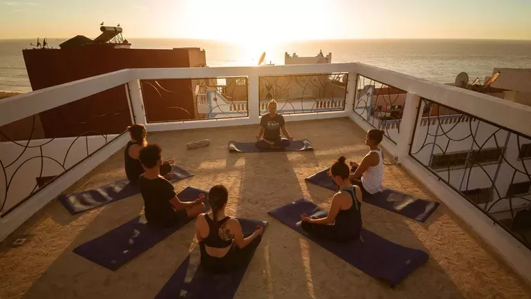 Person praktiziert Yoga auf einer Dachterrasse mit Meerblick im Pure Surfcamp Marokko