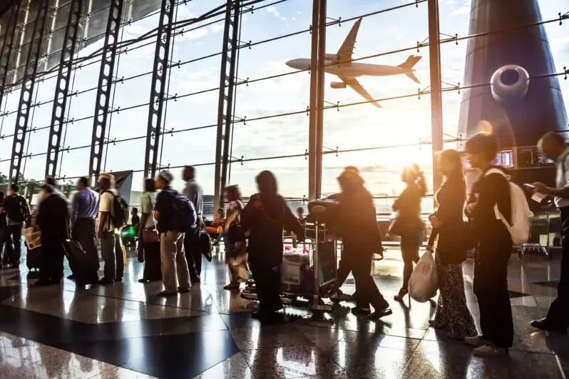 Personen gehen über einen Flughafen-Rollweg mit Flugzeugen im Hintergrund
