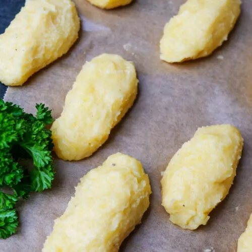 Rohe, geformte Kroketten liegen auf Backpapier bereit zum Panieren.