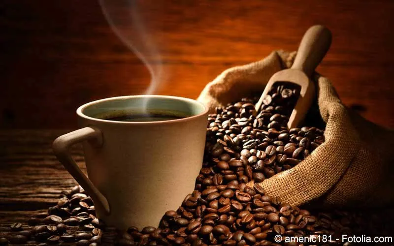 Tasse Kaffee mit Kaffeebohnen auf einem Holztisch, im Hintergrund unscharf