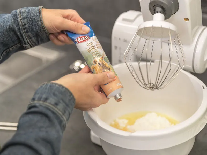 Teig für Hundekekse wird sorgfältig in die Mulden einer Silikon-Backmatte in Knochen- und Herzform gestrichen.